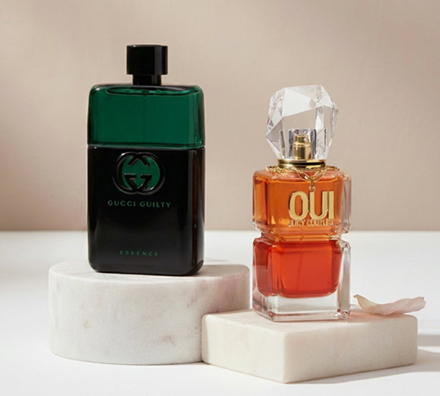 Gucci Guilty Essence and Juicy Couture Oui perfumes displayed on marble podiums with soft lighting.