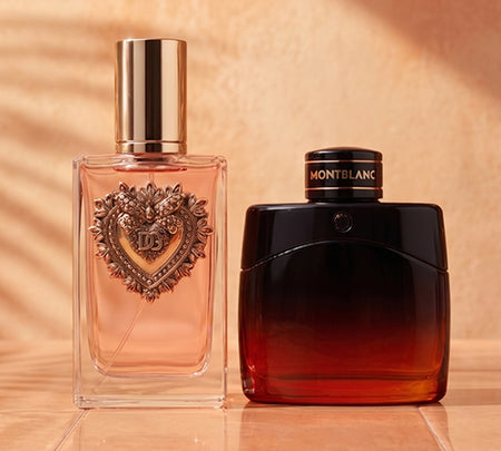 Two fragrance bottles on a warm beige background: a pink Dolce &amp; Gabbana bottle with a gold cap on the left and a black-and-red Montblanc bottle on the right.