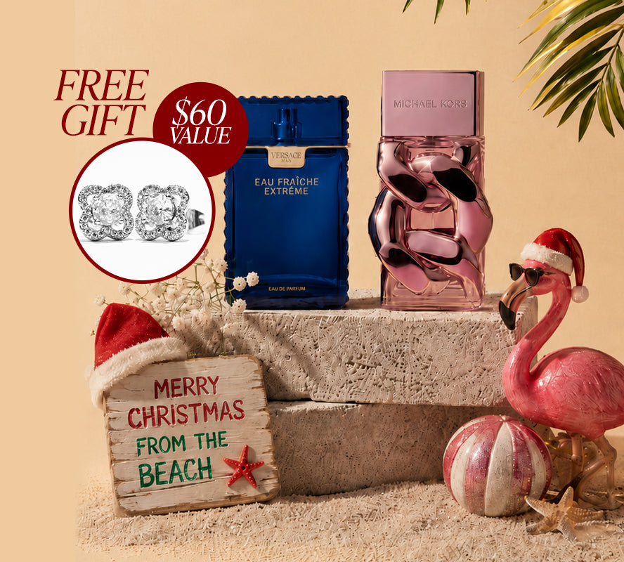 Holiday fragrance display featuring blue Versace and pink Michael Kors perfume bottles on beach-themed décor, with a Santa-hat flamingo, ornaments, a “Merry Christmas from the Beach” sign, and a free $60-value stud earring gift promotion.