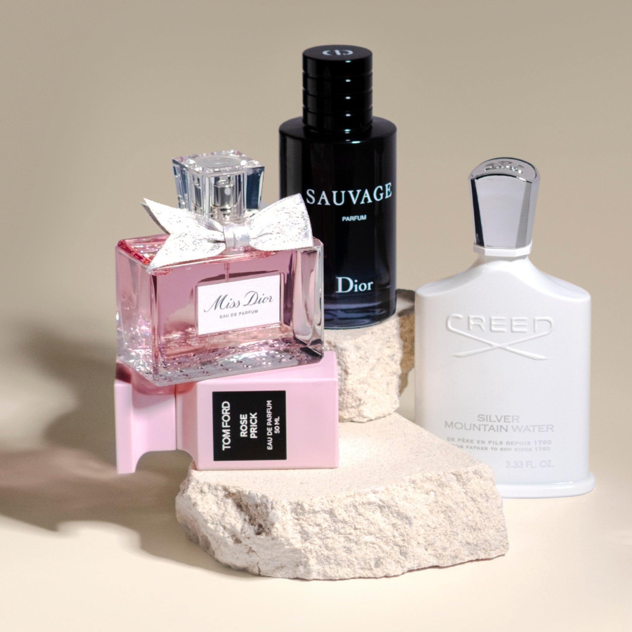 Luxury perfume bottles styled on stone blocks, featuring Miss Dior, Dior Sauvage Parfum, Tom Ford Rose Prick, and Creed Silver Mountain Water.