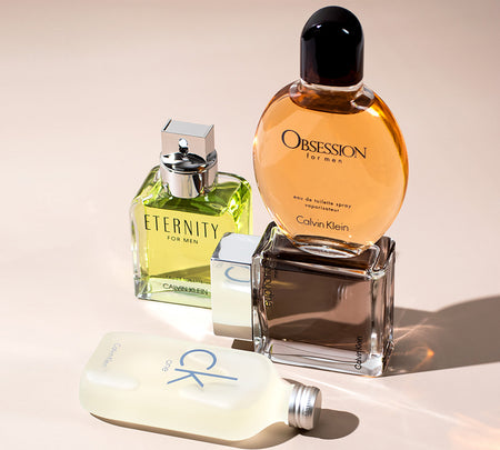 Four Calvin Klein fragrance bottles arranged on a light surface, including Eternity for Men, Obsession for Men, Euphoria Men, and a CK One bottle lying in front.