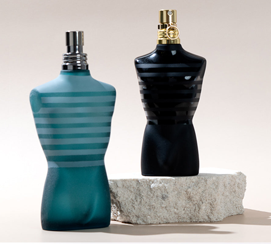 Two torso-shaped cologne bottles—one teal striped, one black—on a stone pedestal.