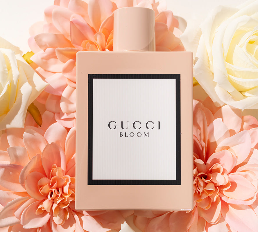 Gucci Bloom perfume bottle surrounded by soft pink and white flowers.