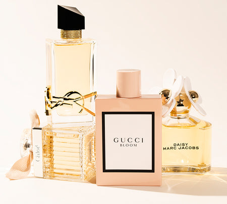 Three women’s perfume bottles arranged on a light surface: Yves Saint Laurent Libre on the left, Gucci Bloom in the center, and Marc Jacobs Daisy on the right.