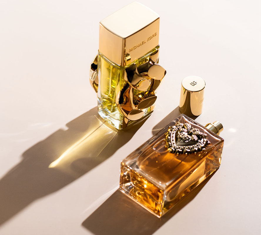 Two gold-toned perfume bottles on a surface, one upright and one lying down with caps nearby.